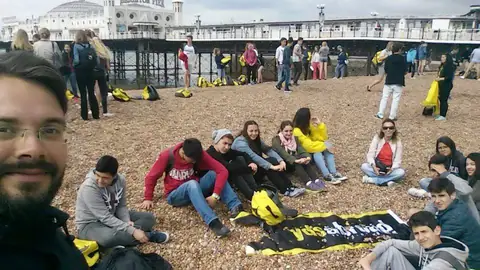 Brighton sahilinde çakılların üstünde oturan öğrenciler