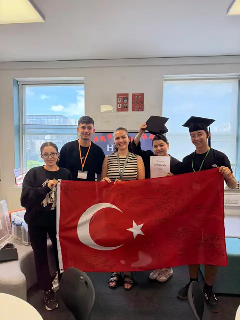 Kep takmış öğrenciler Türk bayrağıyla poz veriyor