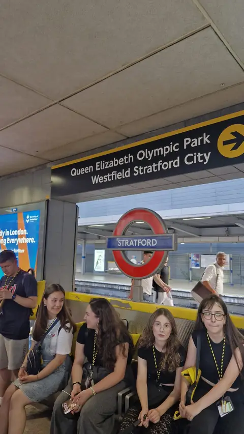 Stratford metro peronunda bankta oturan öğrenciler