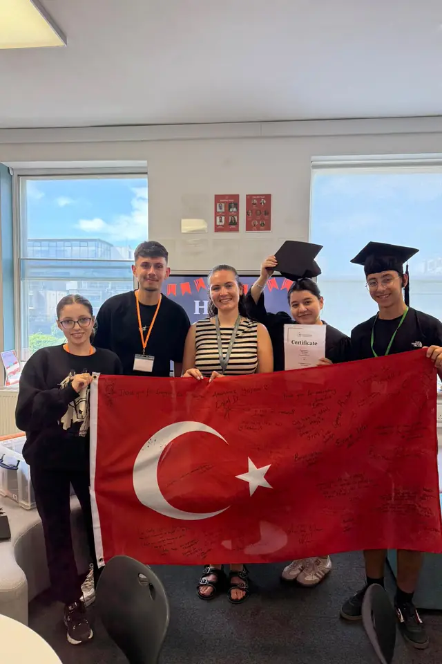 Kep takmış öğrenciler sınıfta Türk bayrağı ve sertifikalarıyla poz veriyor